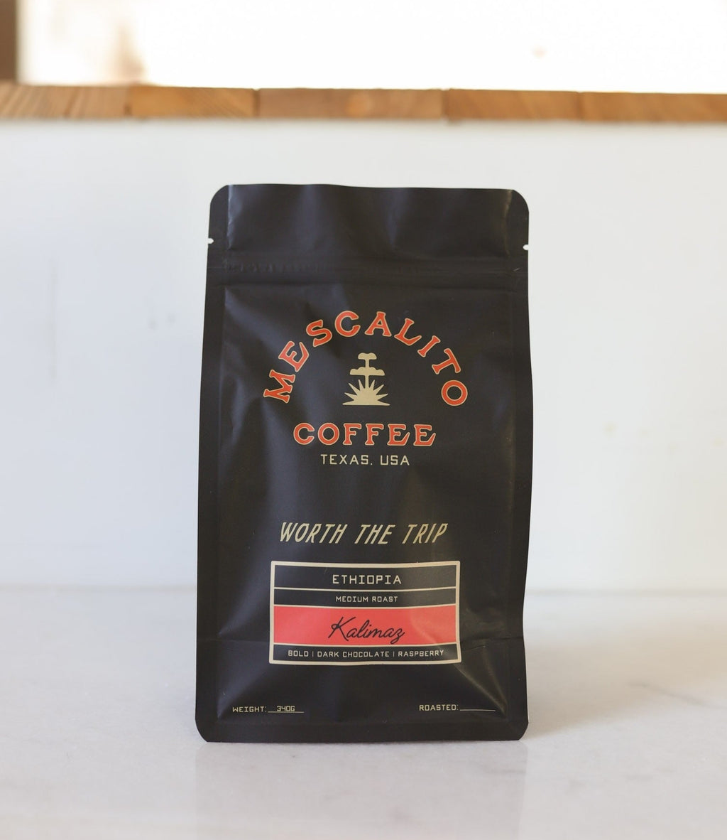 A black bag of Mescalito Coffee's Blend Whole Coffee Beans "Kalimaz" rests on a white surface, featuring bold notes of dark chocolate and raspberry from an extended fermentation process.