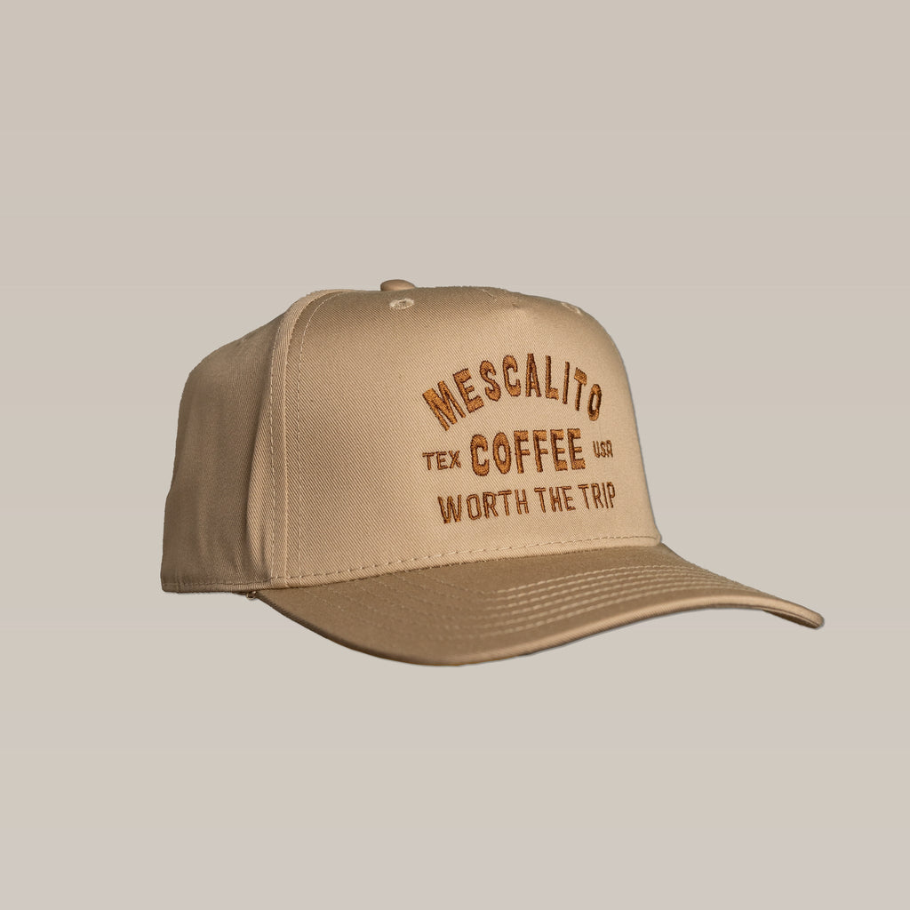 The Mescalito Coffee Shop Hat in tan features "Worth The Trip" embroidered on the front in brown and yellow. This laid-back baseball cap is perfect for coffee lovers and casual outings.