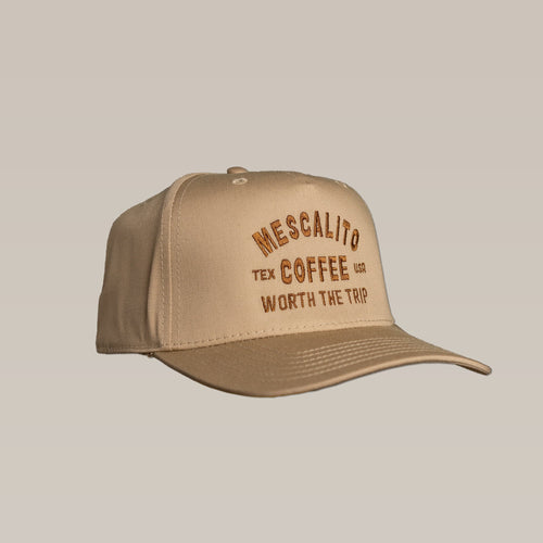 The Mescalito Coffee Shop Hat in tan features "Worth The Trip" embroidered on the front in brown and yellow. This laid-back baseball cap is perfect for coffee lovers and casual outings.